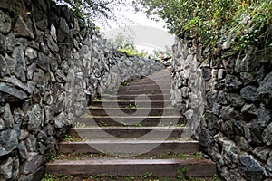 A high staircase with wooden steps extending upward surrounded by stone walls in summer. Travel and mystical places