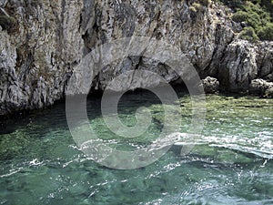 A high stone cliff overhangs the turquoise water of the river. On top of the rock grow low spreading trees