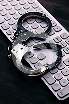 High tech IT cyber crime arrest concept, image of police handcuffs over computer keyboard