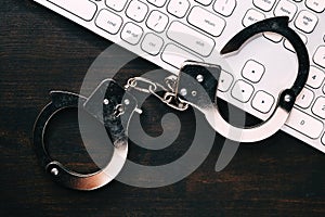 High tech IT cyber crime arrest concept, image of police handcuffs over computer keyboard