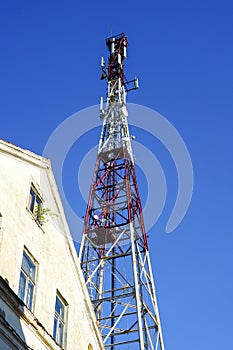 High telecommunication tower in city with TV antennas and satellite dishes on blue sky background