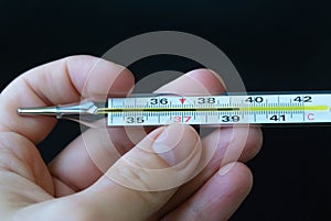 A high temperature thermometer is held in the hand of a woman on a dark background.