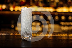 High transparent glass filled with ice cubes on the bar counter of restaurant in blurred background