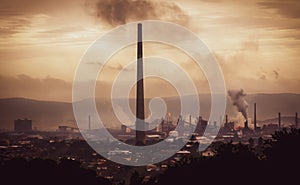 High view across industrial town to steel works and smoke stacks on stormy atmospheric evening. Old industries, climate change and photo