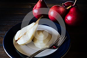 High view of a halved, unpeeled red battler pear on a plate and other pears on the table. Dark background. Organic and natural