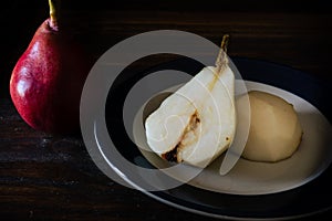 High view of a halved, unpeeled red battler pear on a plate and other pears on the table. Dark background. Organic and natural