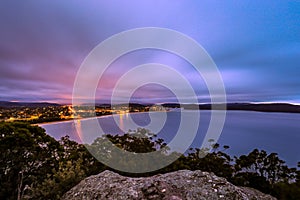 High view of ocean and city night lights against cloudy sunrise