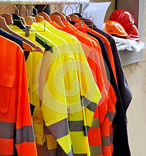 High visibility jackets on a hanger with protective helmets behind, in a work clothes store