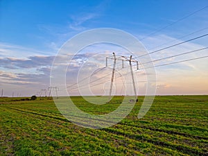 High voltage electric poles, rural landscape with power pylons in a row, at sunset