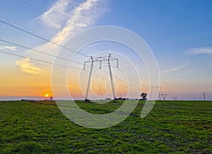 High voltage electric poles, rural landscape with power pylons in a row, at sunset