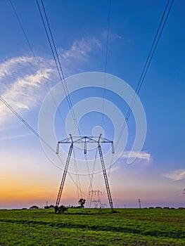 High voltage electric poles, rural landscape with power pylons in a row, at sunset