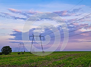 High voltage electric poles, rural landscape with power pylons in a row, at sunset