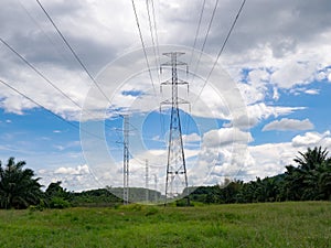 High voltage electric power pole in green field against with blue sky white cloud