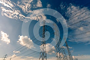 High voltage electric pylon and electrical wire against blue sky and white clouds. Bottom view of Electricity pylon with sunlight