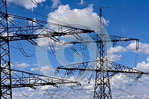 High voltage and electric pylons against sky with clouds