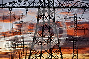 High voltage and electric pylons against sky with clouds