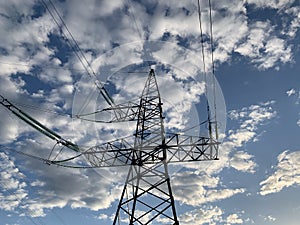 High voltage electric tower against the blue sky. High steel power pole, among the forest. High voltage electrical wires pass