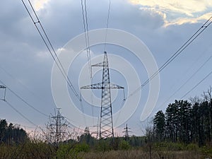 High voltage electric tower against a cloudy sky. High steel power pole, among the forest