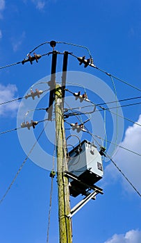 High voltage electrical power cables and transformer seen erected on a wooden pole.