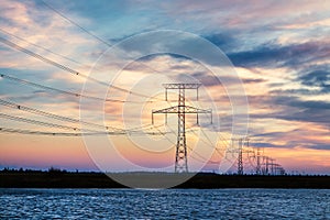 High voltage electricity lines over river at sunset