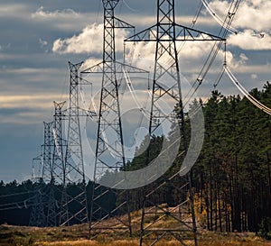 High voltage electricity power line towers near forest. Cloudy sky. Transmission towers