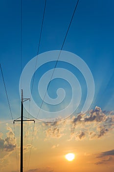 High voltage electricity pylons against beautiful sky with sun rays. Electric pole power lines and clouds.