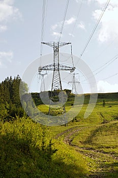 High voltage eletrical towers and lines with blue sky and green meadow. Eletricity towers on a green field. Transmission towers.