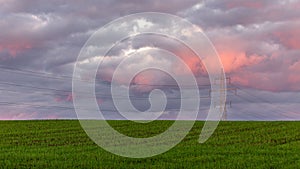 High voltage line in a green farmland against cloudy sky at sunset