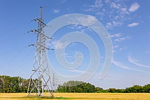 High voltage line with pillars against the background of the field, forest and sky. Summer photo