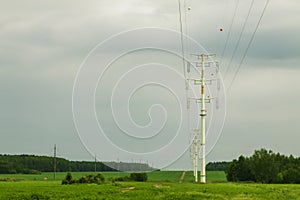 High voltage line with pillars against the background of the forest, field and sky.