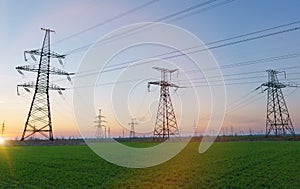 High voltage lines and power poles and green agricultural landscape during sunset