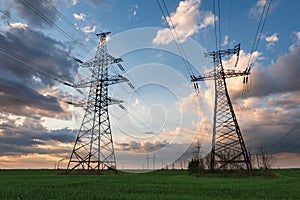 High voltage lines and power poles and green agricultural landscape during sunset