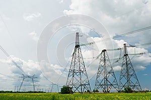 High voltage lines and power poles and green agricultural landscape during sunset