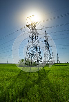 High voltage lines and power pylons in a flat and green agricultural landscape on a sunny day with clouds in the blue sky