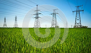 High voltage lines and power pylons in a flat and green agricultural landscape on a sunny day with clouds in the blue sky