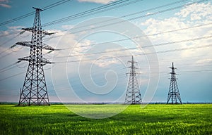 High voltage lines and power pylons in a flat and green agricultural landscape on a sunny day with clouds in the blue sky. Cloudy