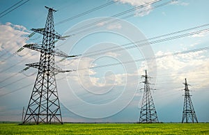 High voltage lines and power pylons in a flat and green agricultural landscape on a sunny day with clouds in the blue sky. Cloudy