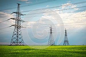 High voltage lines and power pylons in a flat and green agricultural landscape on a sunny day with clouds in the blue sky. Cloudy