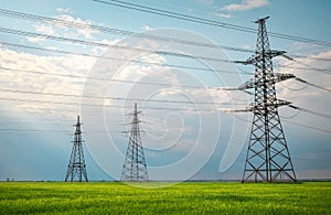 High voltage lines and power pylons in a flat and green agricultural landscape on a sunny day with clouds in the blue sky. Cloudy