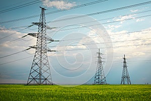 High voltage lines and power pylons in a flat and green agricultural landscape on a sunny day with clouds in the blue sky. Cloudy