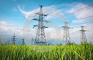 High voltage lines and power pylons in a flat and green agricultural landscape on a sunny day with clouds in the blue sky. Cloudy