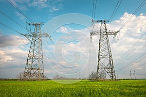 High voltage lines and power pylons in a flat and green agricultural landscape on a sunny day with clouds in the blue sky. Cloudy