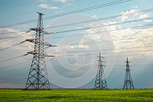 High voltage lines and power pylons in a flat and green agricultural landscape on a sunny day with clouds in the blue sky. Cloudy