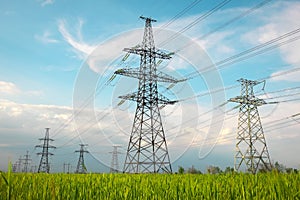 High voltage lines and power pylons in a flat and green agricultural landscape on a sunny day with clouds in the blue sky. Cloudy