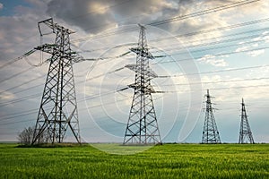 High voltage lines and power pylons in a flat and green agricultural landscape on a sunny day with clouds in the blue sky. Wheat