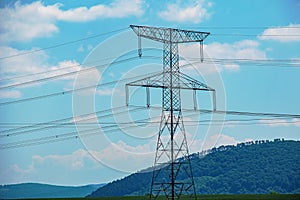 High voltage lines and power pylons in a green landscape on a sunny day with clouds in the blue sky