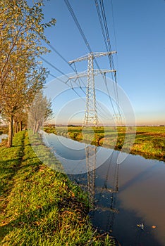 High-voltage lines and pylons reflected in a Dutch polder landscape