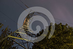 High voltage post or tower up view with tree and night sky clouds. Long exposure photography