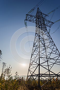 High voltage power line against the blue sky and bright sun