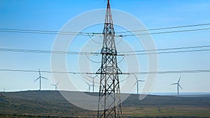 High voltage power line against rotating windmill wind turbines in valley. Concept of green electricity, renewable power and